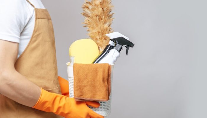 side-view-close-up-hand-young-man-apron-rubber-gloves-holding-basket-cleaning-equipment-feather-duster-spray-bottle-sponge-cloth-wiping-basket_1150-48118